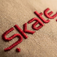 Macro de la broderie rouge Skate sur le sergé de coton beige de la casquette