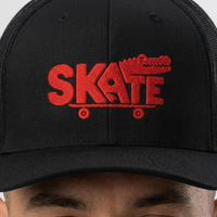 Gros plan sur la broderie rouge SKATE crocodile de la casquette trucker portée