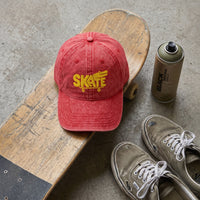 Casquette skate vintage rouge originale posée à plat sur un skateboard, flat lay streetwear