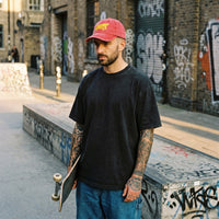 Homme skateur en look streetwear portant la casquette skate vintage rouge brodée crocodile