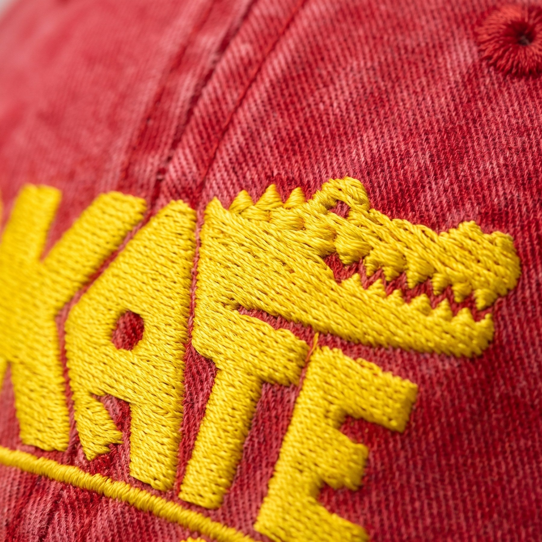 Macro de la broderie crocodile jaune fil à fil sur le sergé de coton rouge délavé