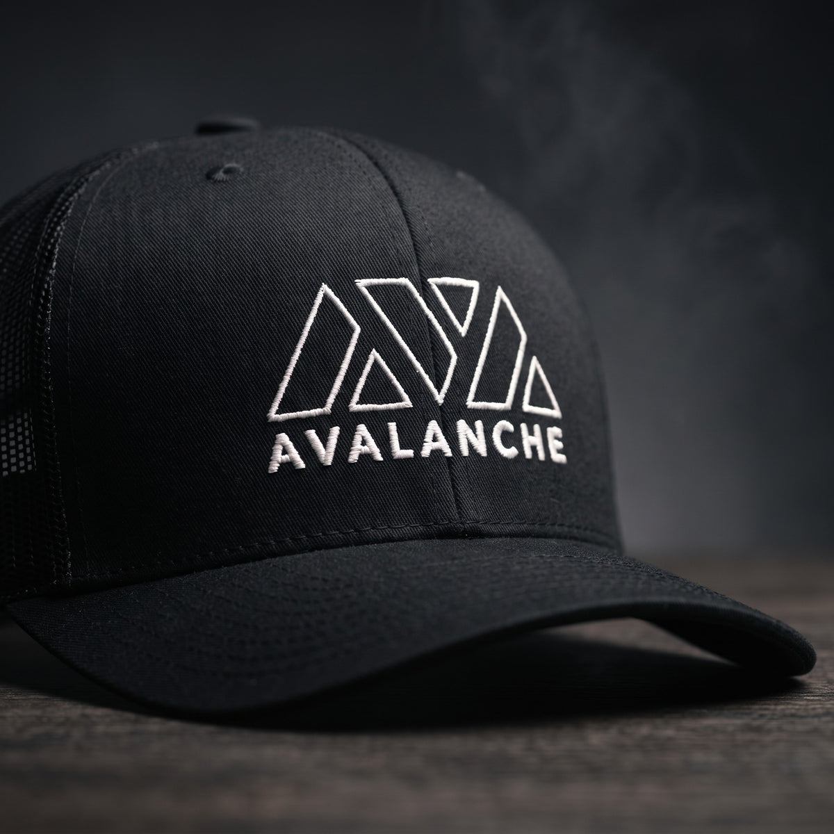 Gros plan sur le logo Avalanche brodé en blanc de la casquette trucker AVAX noire