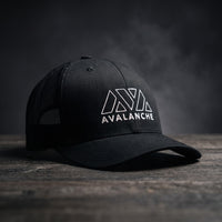 Casquette trucker AVAX Avalanche noire avec logo brodé blanc et mot AVALANCHE, filet noir, posée sur bois sombre