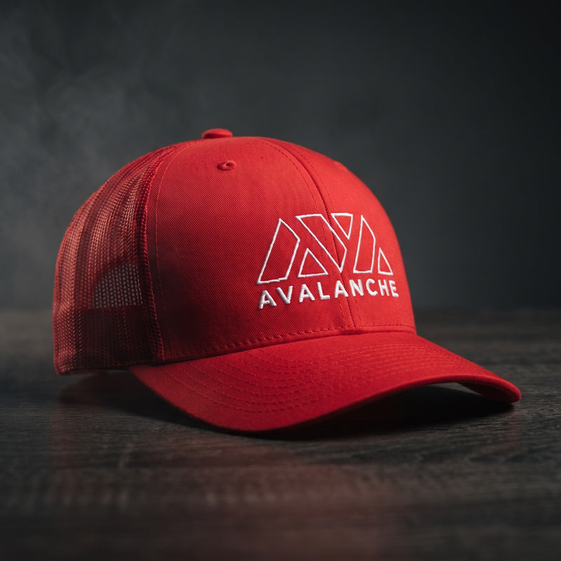 Casquette trucker AVAX Avalanche rouge sur un bureau de trader crypto de nuit devant des écrans de graphiques