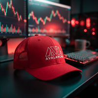 Casquette trucker AVAX Avalanche rouge avec logo brodé blanc et mot AVALANCHE, filet rouge, posée sur bois sombre