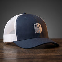Casquette trucker brodée hibou Coolawls bleu marine et blanc, vue trois-quarts sur fond bois