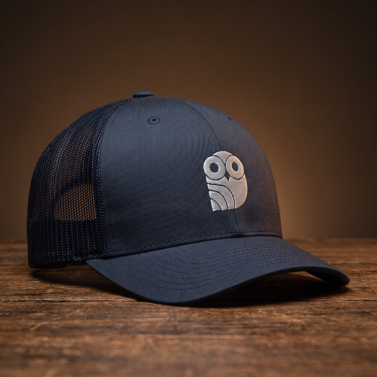 Casquette trucker brodée hibou Coolawls bleu marine, vue trois-quarts sur fond bois