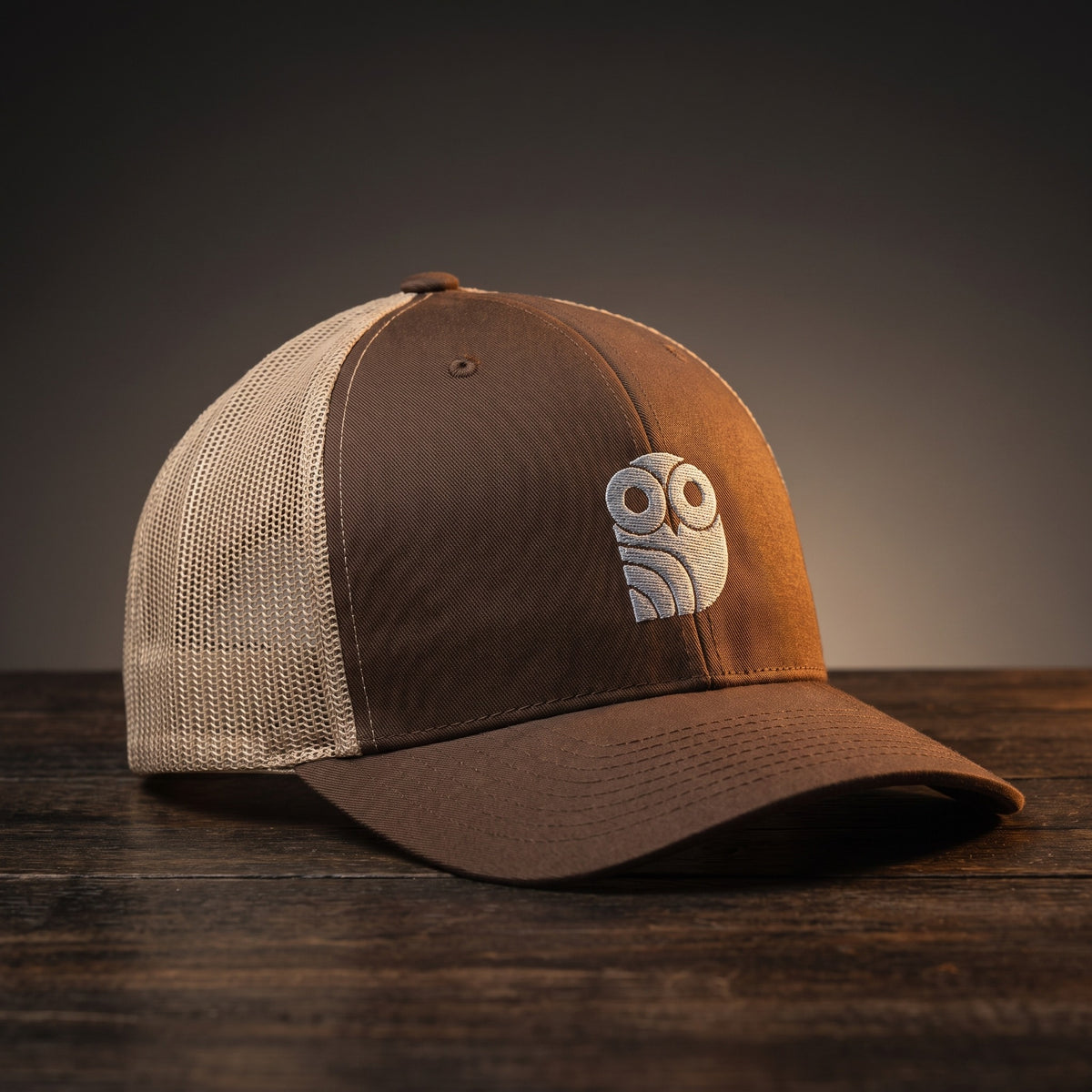 Casquette trucker brodée hibou Coolawls marron et kaki, vue trois-quarts sur fond bois
