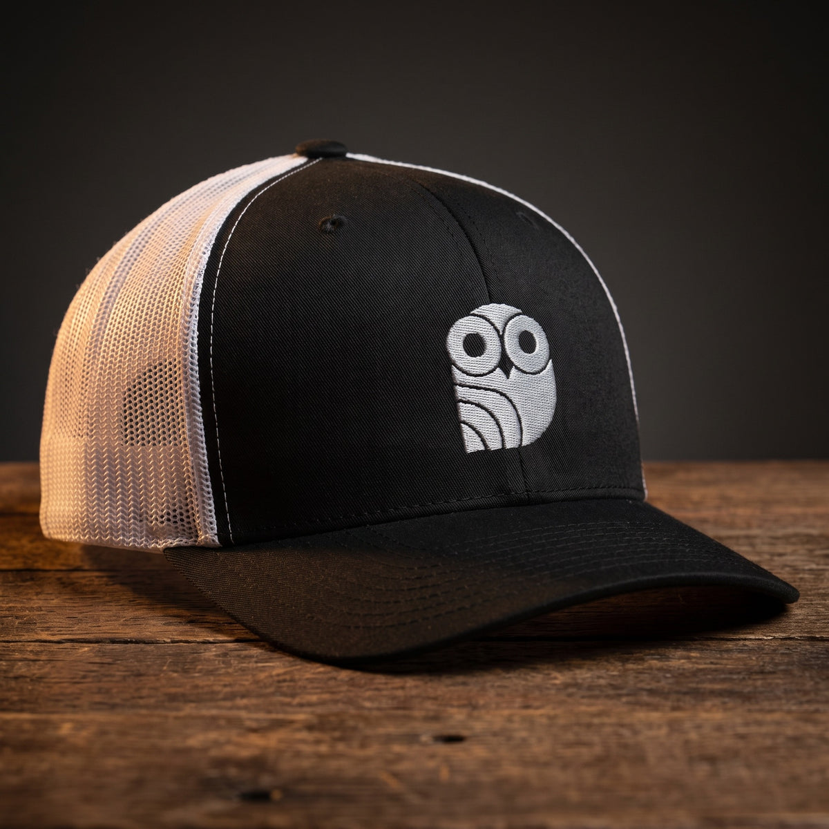 Casquette trucker brodée hibou Coolawls noir et blanc, vue trois-quarts sur fond bois