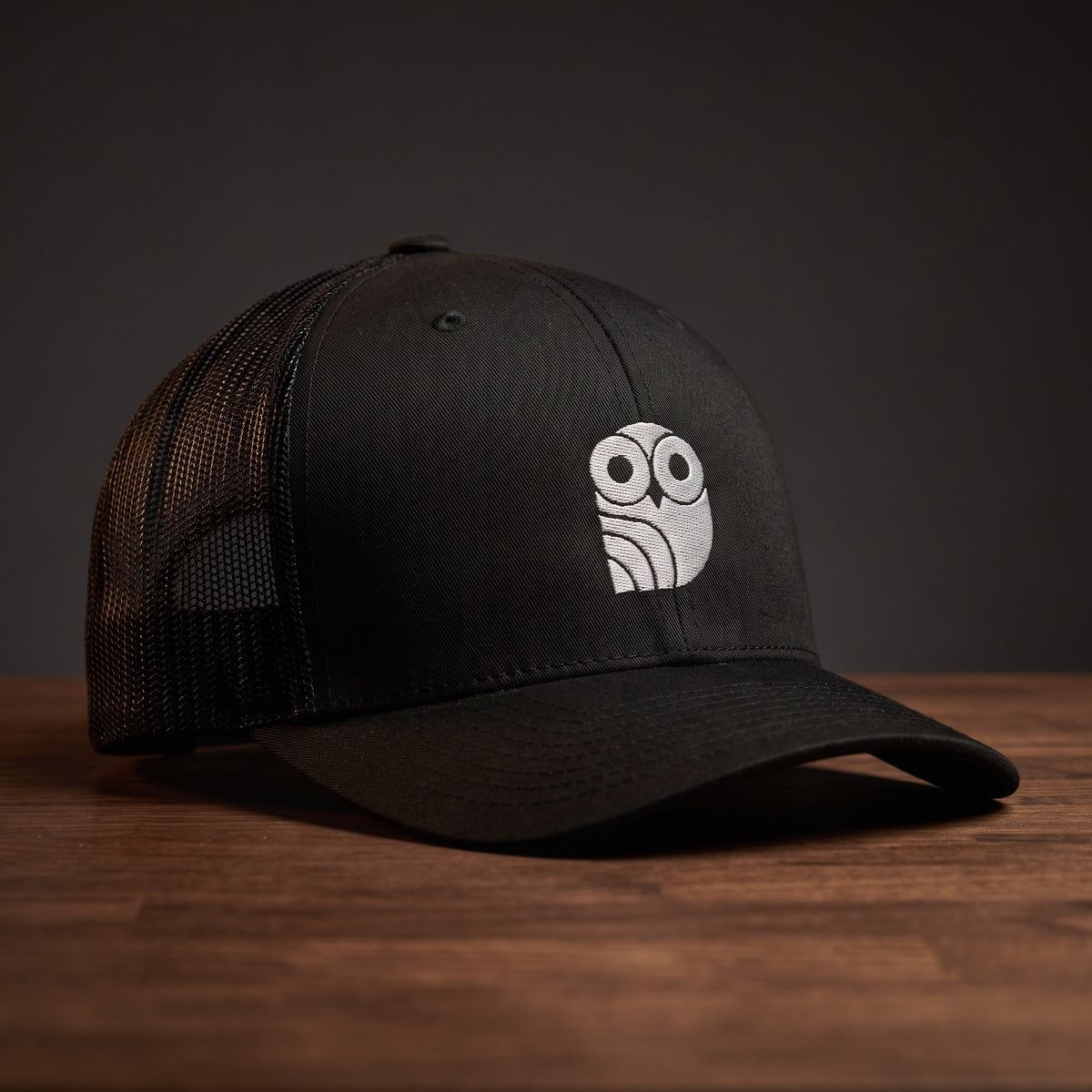 Casquette trucker brodée hibou Coolawls noire, vue trois-quarts sur fond bois