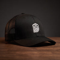 Casquette trucker brodée hibou Coolawls noire, vue trois-quarts sur fond bois