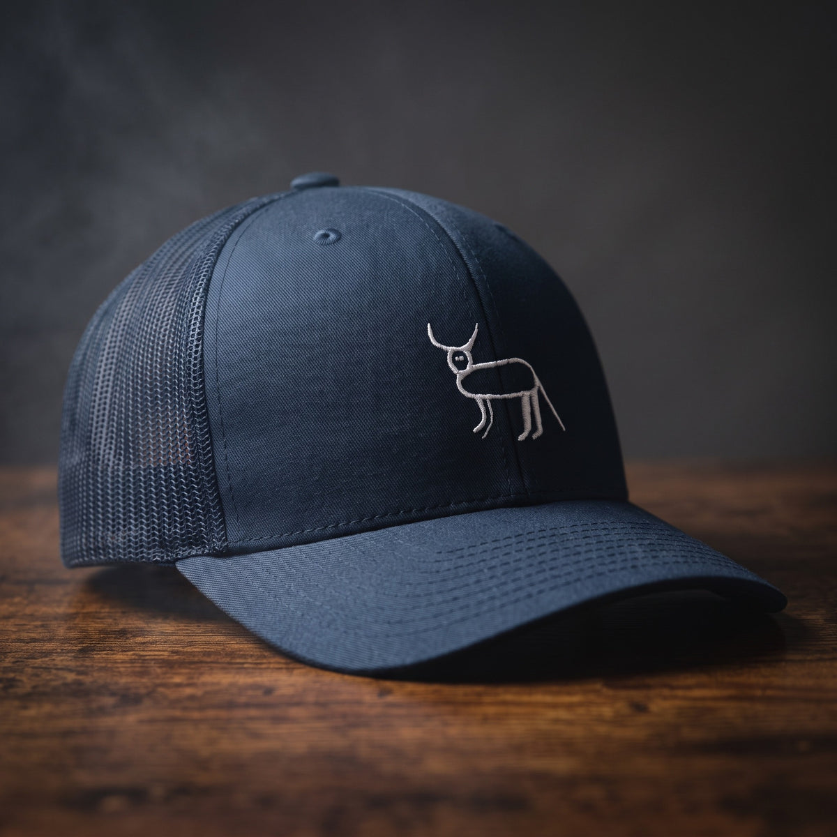 Casquette trucker bleu marine avec la perruche ratée brodée en blanc, posée sur un bois sombre