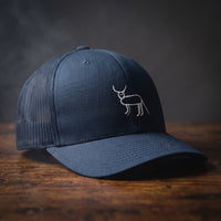 Casquette trucker bleu marine avec la perruche ratée brodée en blanc, posée sur un bois sombre