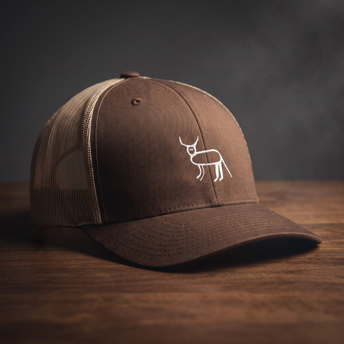 Casquette trucker marron et kaki avec la perruche ratée brodée en blanc, posée sur un bois sombre