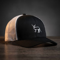 Casquette trucker noire et blanche avec la perruche ratée brodée en blanc, posée sur un bois sombre