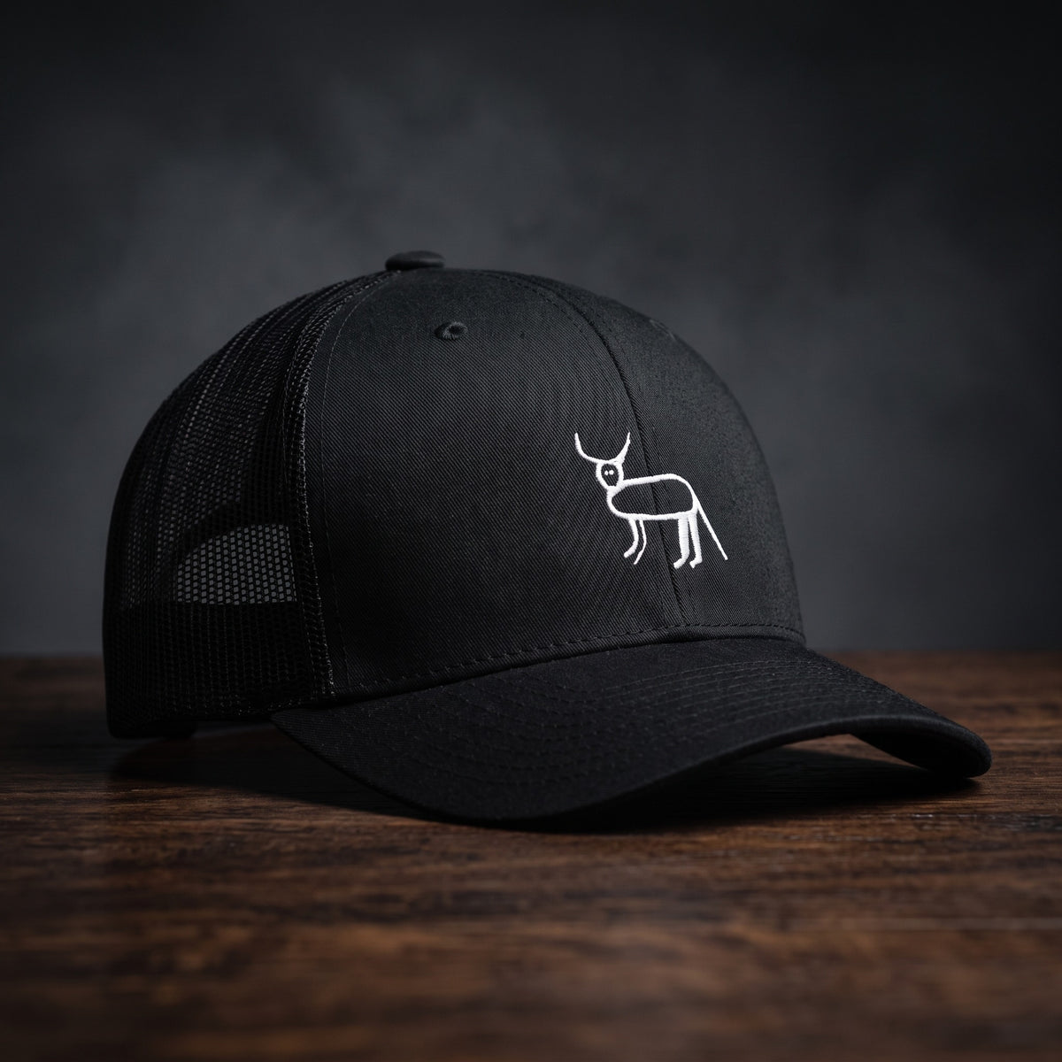 Casquette trucker noire avec la perruche ratée brodée en blanc sur le devant, posée sur un bois sombre