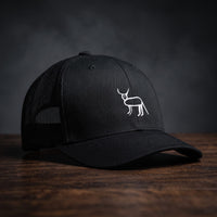 Casquette trucker noire avec la perruche ratée brodée en blanc sur le devant, posée sur un bois sombre