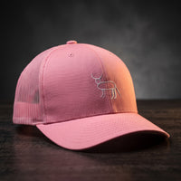 Casquette trucker rose avec la perruche ratée brodée en blanc, posée sur un bois sombre