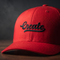Gros plan sur la broderie noire en relief du mot Create sur une casquette trucker rouge