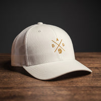 Casquette trucker brodée DAD blanche posée sur bois – logo chope de bière doré
