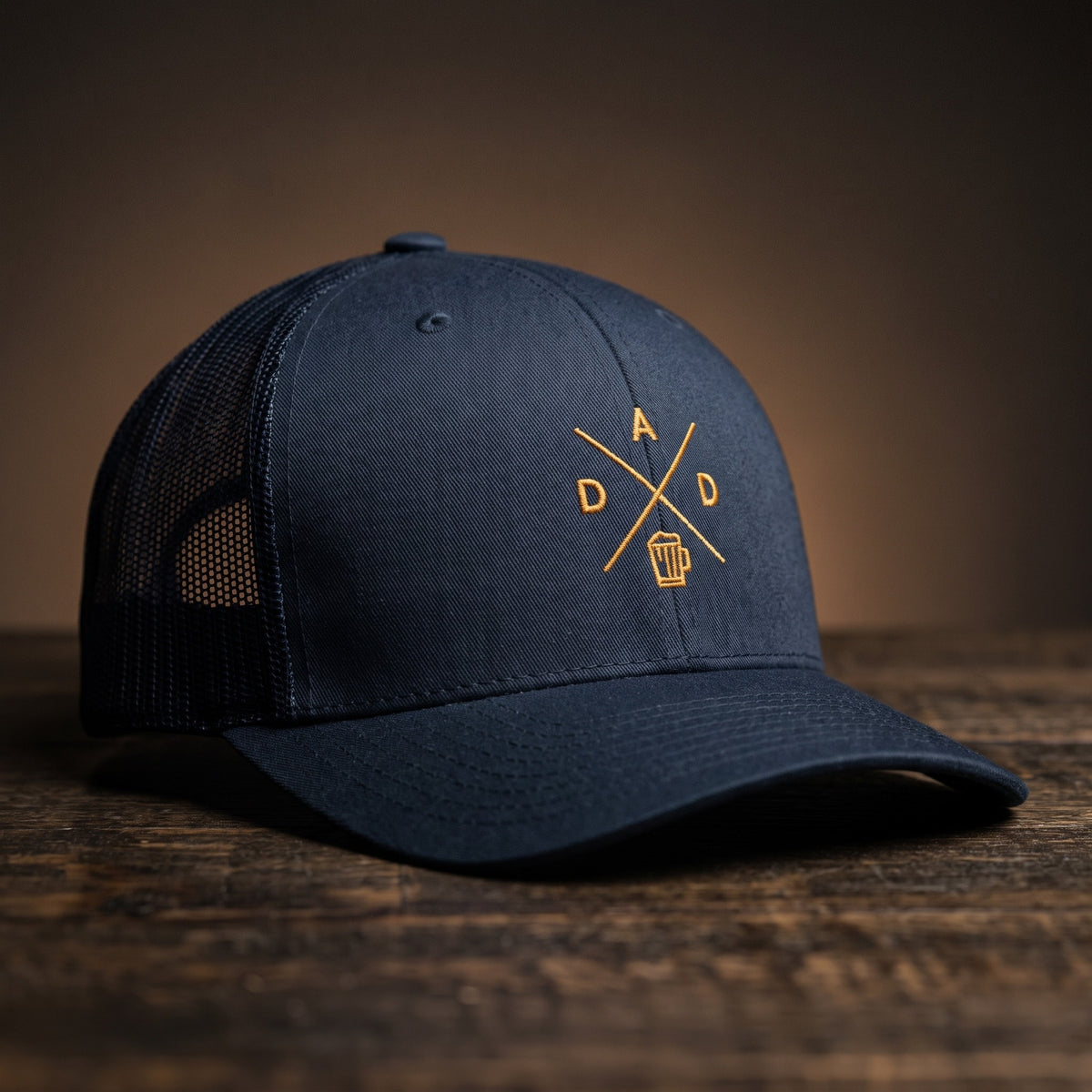 Casquette trucker brodée DAD bleu marine posée sur bois – logo chope de bière doré