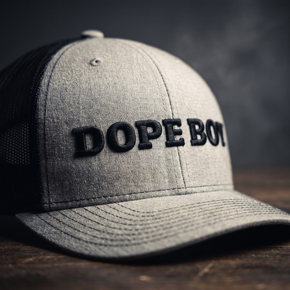 Gros plan sur la broderie noire DOPE BOY en relief sur une casquette trucker gris chiné