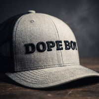 Gros plan sur la broderie noire DOPE BOY en relief sur une casquette trucker gris chiné