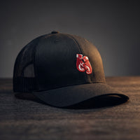 Casquette trucker noire avec gants de boxe rouges brodés, posée sur un plan de bois sombre