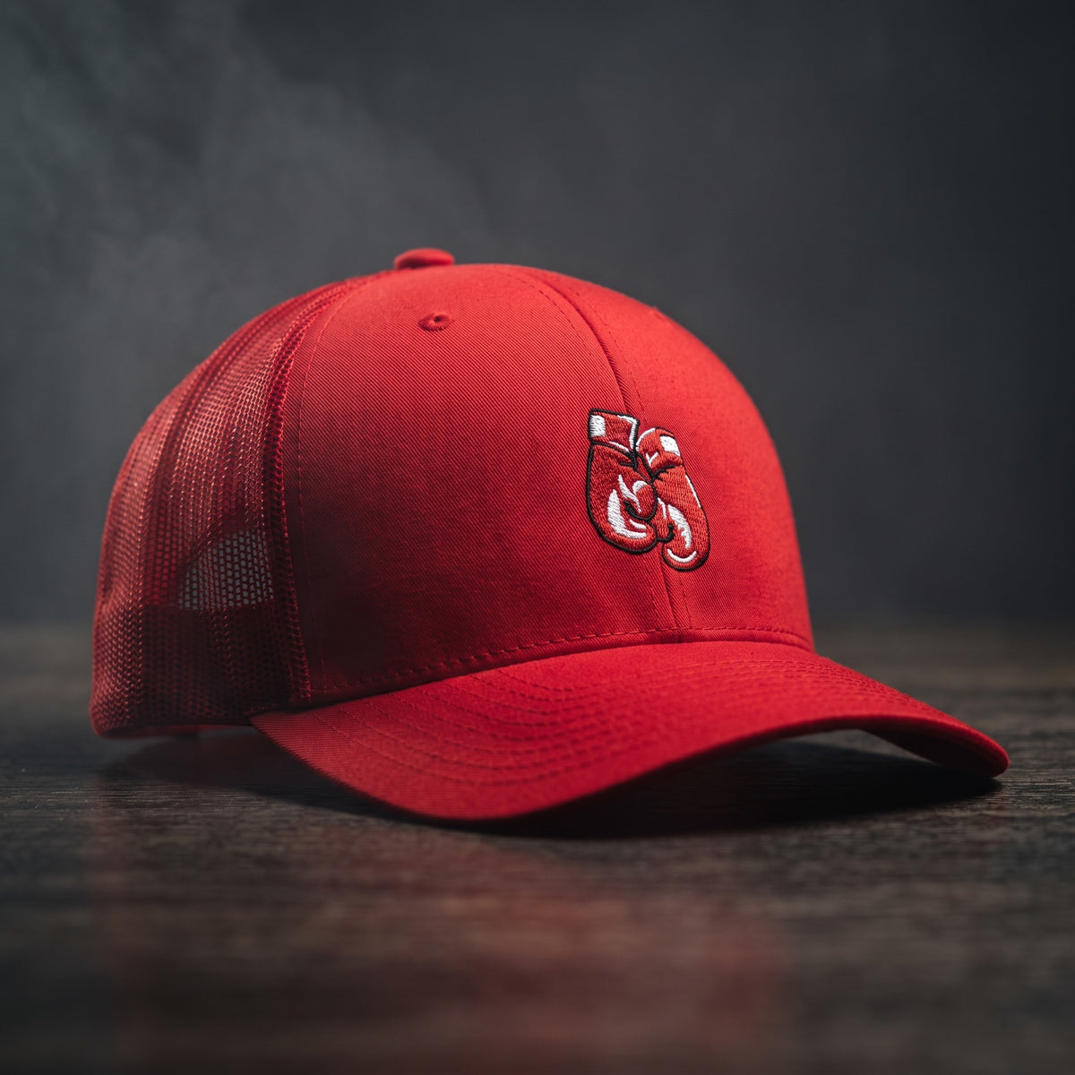 Casquette trucker rouge avec gants de boxe brodés, posée sur un plan de bois sombre