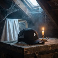 Casquette trucker GHOST noire sur une vieille malle dans un grenier hanté avec bougie et drap blanc