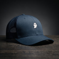 Casquette trucker GHOST bleu marine avec petit fantôme blanc brodé, posée sur bois sombre