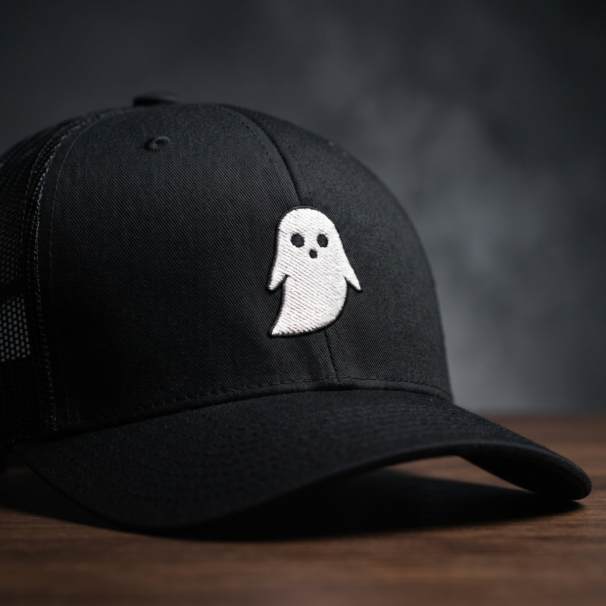 Gros plan sur le logo fantôme blanc brodé de la casquette trucker GHOST noire