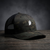Casquette trucker GHOST camouflage multicam noir avec fantôme blanc brodé, filet noir, sur bois sombre