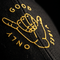 Macro de la broderie fil doré shaka Good Vibes Only sur la casquette trucker noire