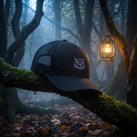 Casquette trucker Hiboux Origami noire posée dans une forêt nocturne brumeuse avec lanterne, ambiance CHT'M Boutique