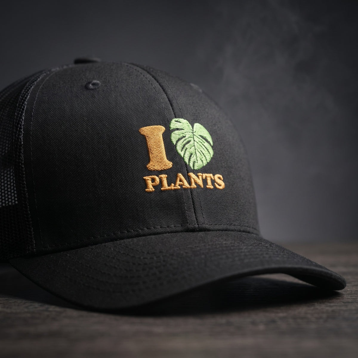 Gros plan sur la broderie I LOVE PLANTS : cœur en feuille de monstera verte et lettres ocre sur casquette trucker noire