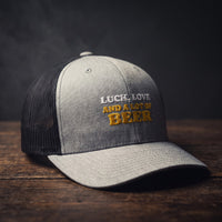 Casquette trucker gris chiné avec filet noir brodée « Luck, Love and a lot of Beer » en blanc et jaune doré
