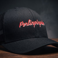 Gros plan sur la broderie Perlinpinpin en script rétro rouge et blanc sur une casquette trucker noire