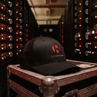 Casquette trucker noire REDSYSTEM posée sur une flight case dans un data center