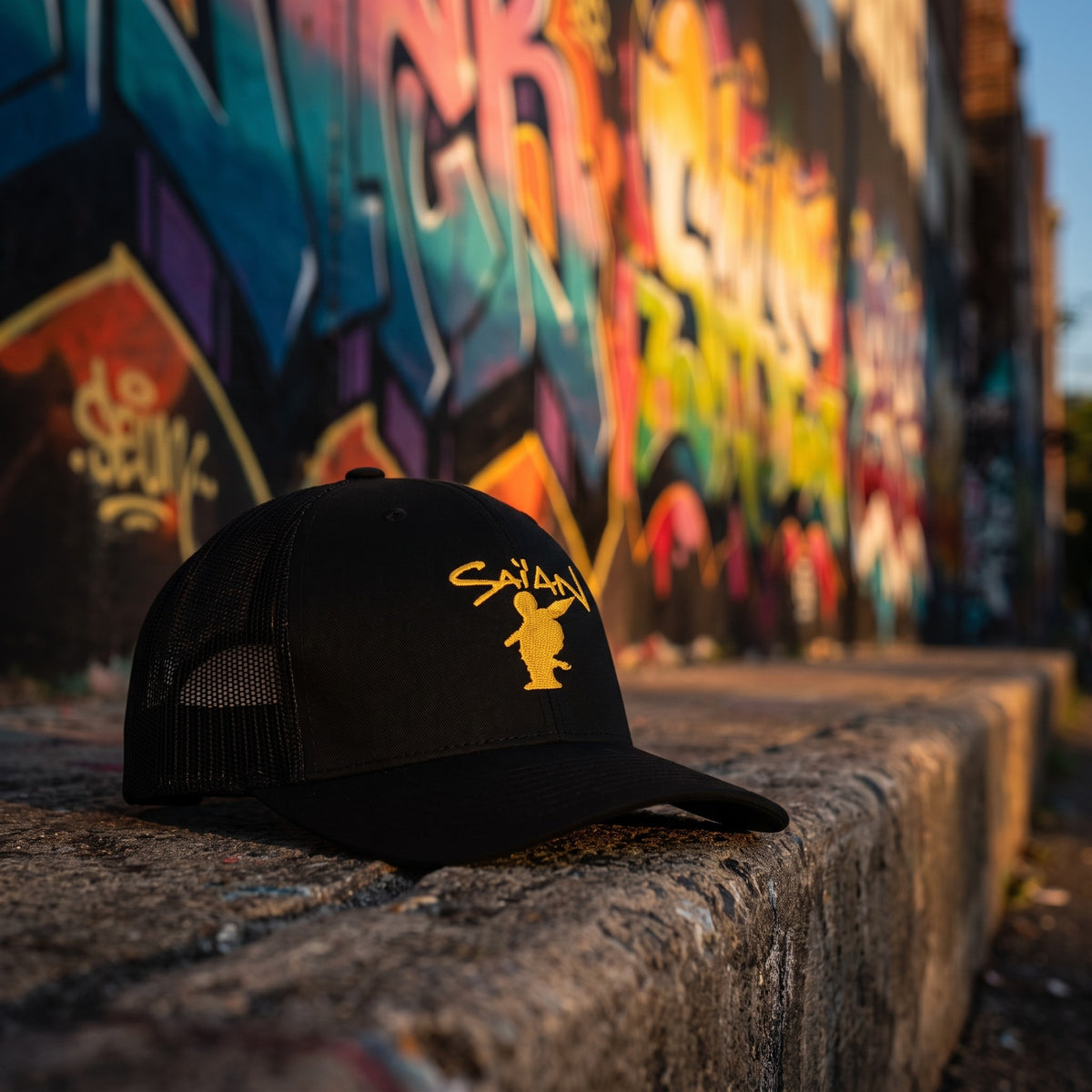 Casquette trucker Saïan Supa Crew posée sur un muret devant un mur de graffitis dans une ruelle