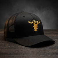Casquette trucker noire brodée Saïan Supa Crew, lettrage jaune or, posée sur un bois sombre