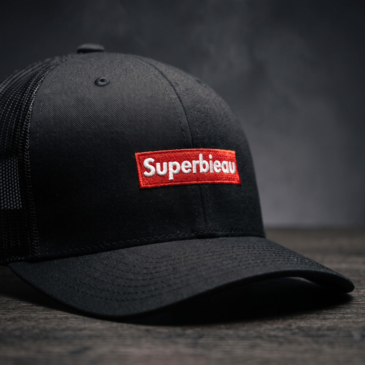 Détail du patch rouge brodé Superbieau sur casquette trucker noire
