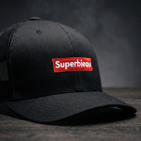 Détail du patch rouge brodé Superbieau sur casquette trucker noire