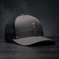 Casquette trucker Thunder Skull gris anthracite avec filet noir et crâne éclair brodé, posée sur bois sombre