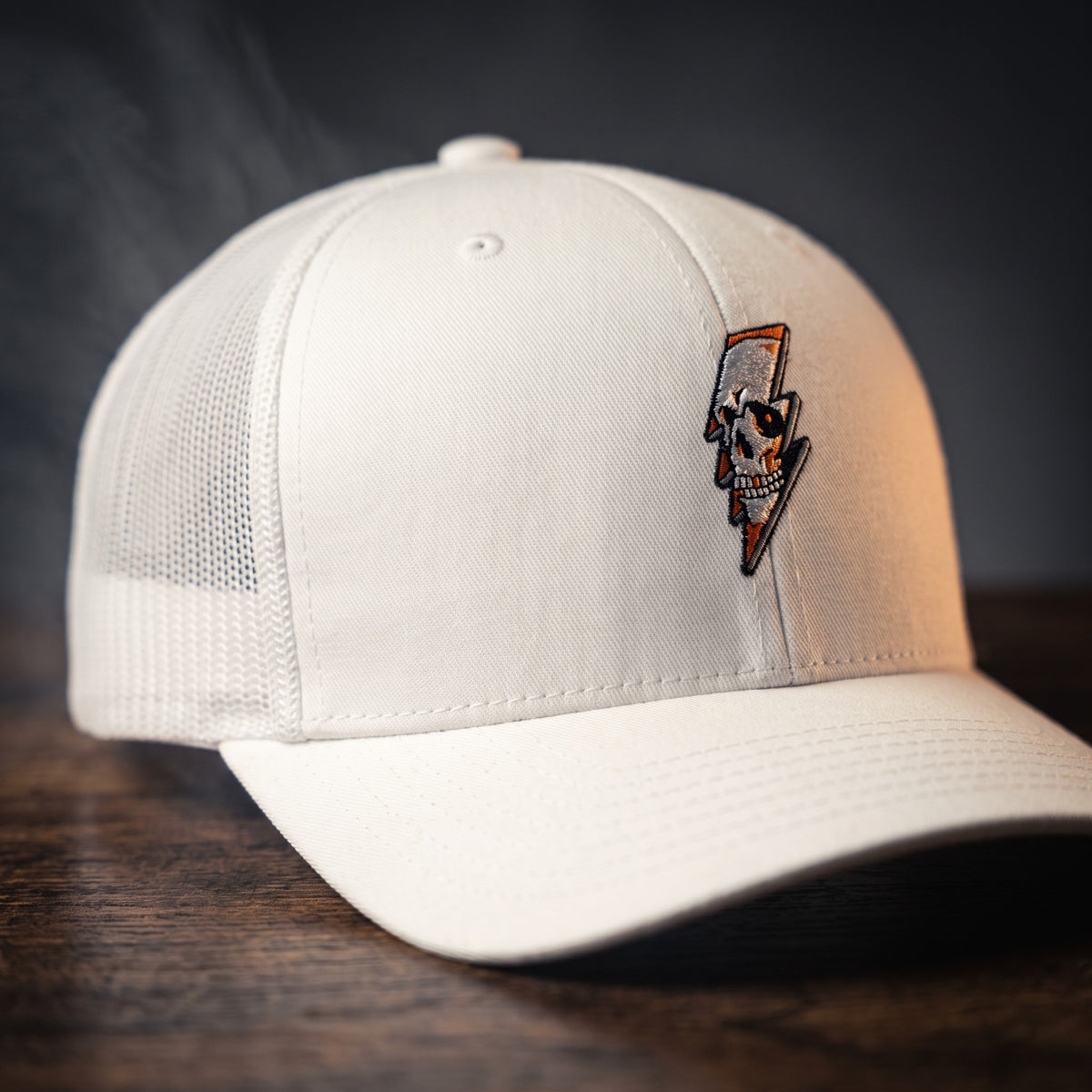 Casquette trucker Thunder Skull blanche avec crâne et éclair brodés, posée sur bois sombre