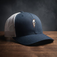 Casquette trucker Thunder Skull bleu marine et blanche avec crâne et éclair brodés, filet blanc, posée sur bois sombre