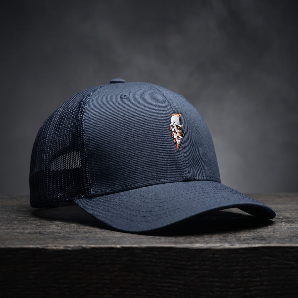 Casquette trucker Thunder Skull bleu marine avec crâne et éclair brodés, posée sur bois sombre