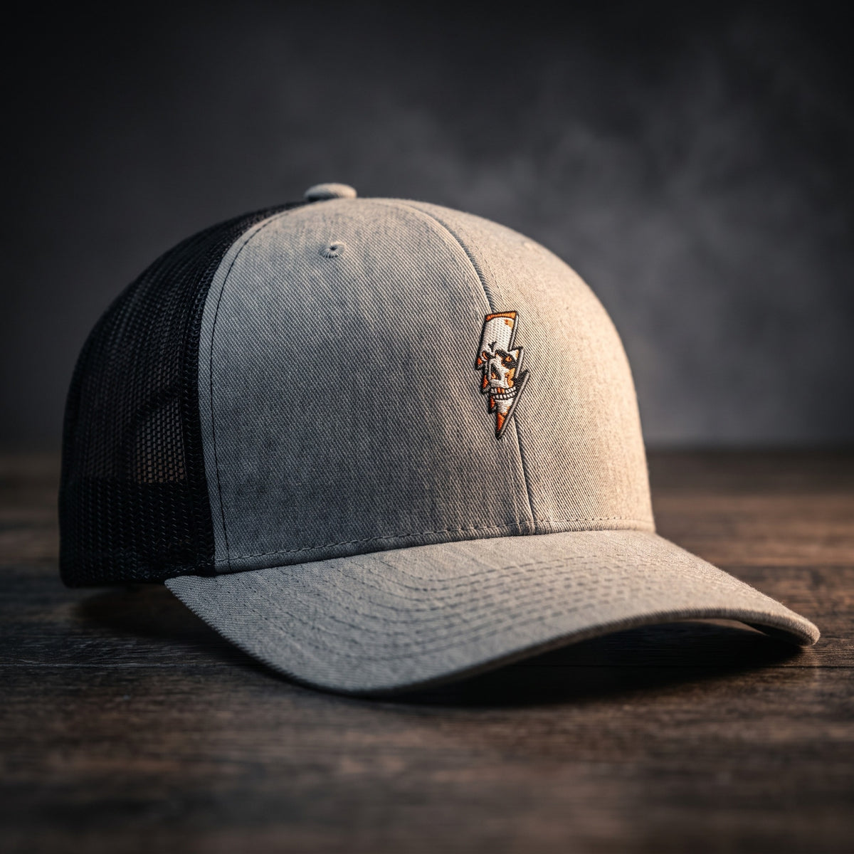 Casquette trucker Thunder Skull gris chiné avec filet noir et crâne éclair brodé, posée sur bois sombre