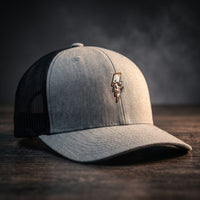 Casquette trucker Thunder Skull gris chiné avec filet noir et crâne éclair brodé, posée sur bois sombre