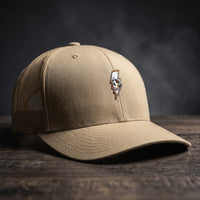Casquette trucker Thunder Skull kaki sable avec crâne et éclair brodés, posée sur bois sombre
